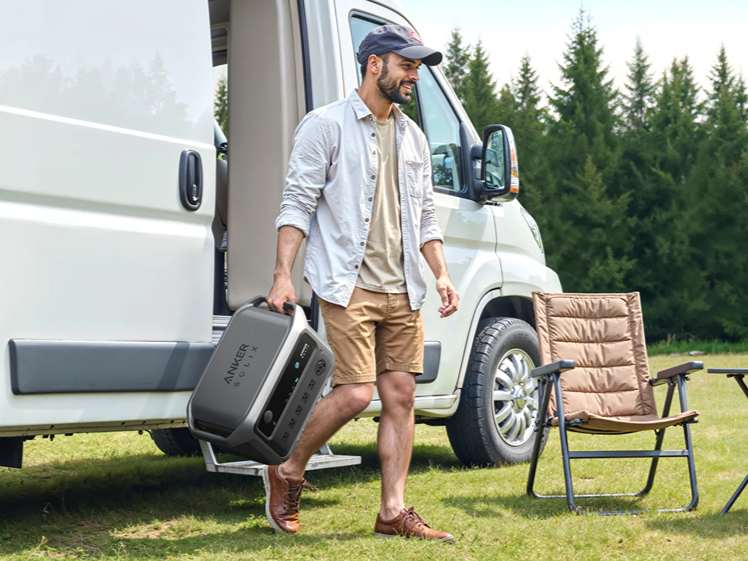 Man carrying a portable power station beside an RV